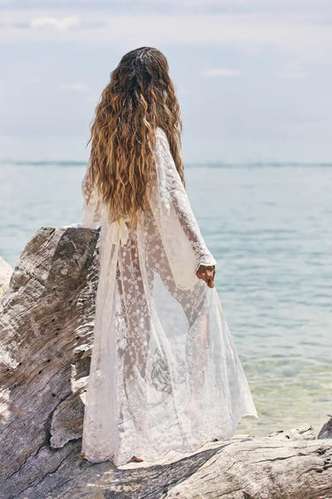 Woman in a white dress standing on rocks by the water